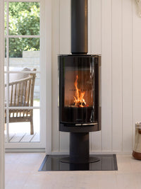Side view of Aduro 22.3 Lux wood burning stove with glossy glass door and elegant pedestal design in a modern setting.