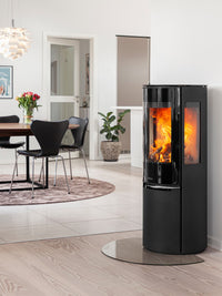 Tall black wood burning stove with glass door, elevated combustion chamber, and sleek design, perfect for small spaces.