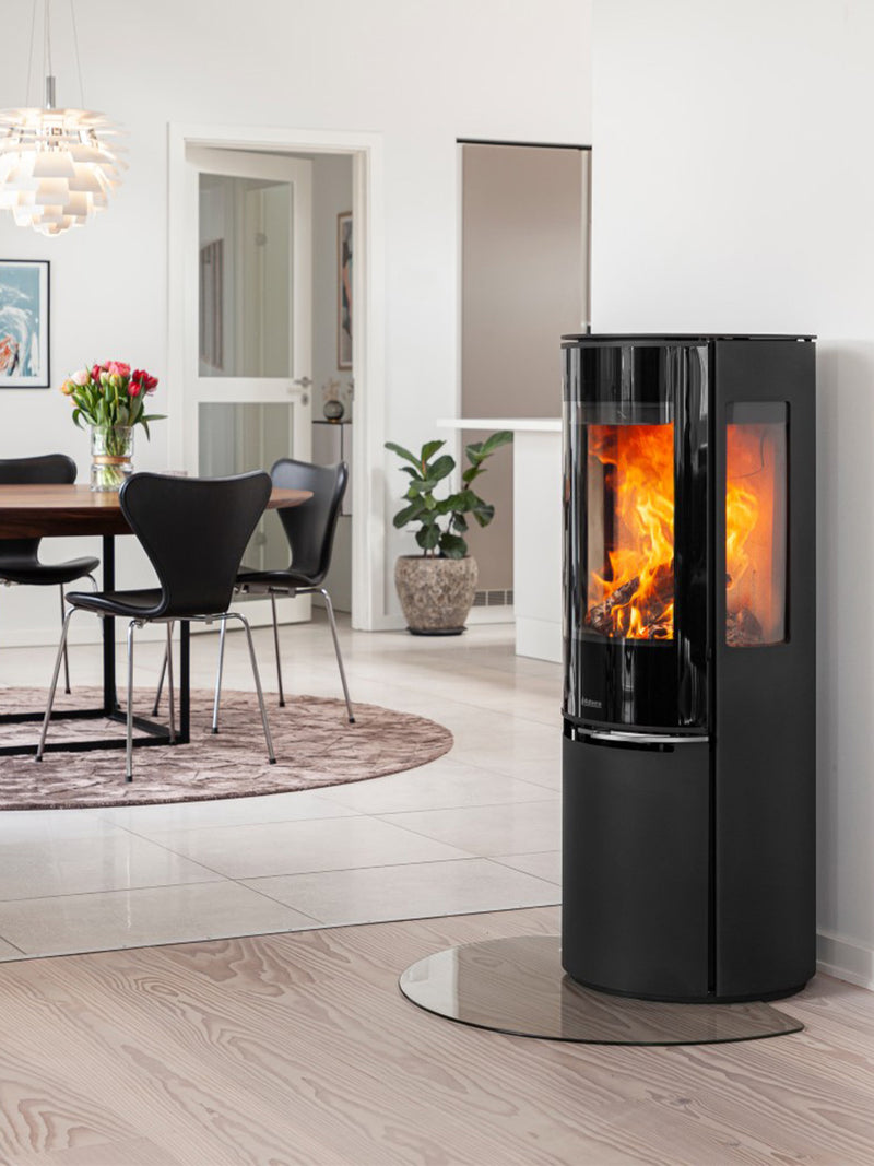 Tall black wood burning stove with glass door, elevated combustion chamber, and sleek design, perfect for small spaces.