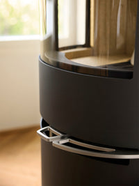 Side view of Aduro H1 Hybrid Stove showcasing large glass area and sleek black finish with logs burning inside.