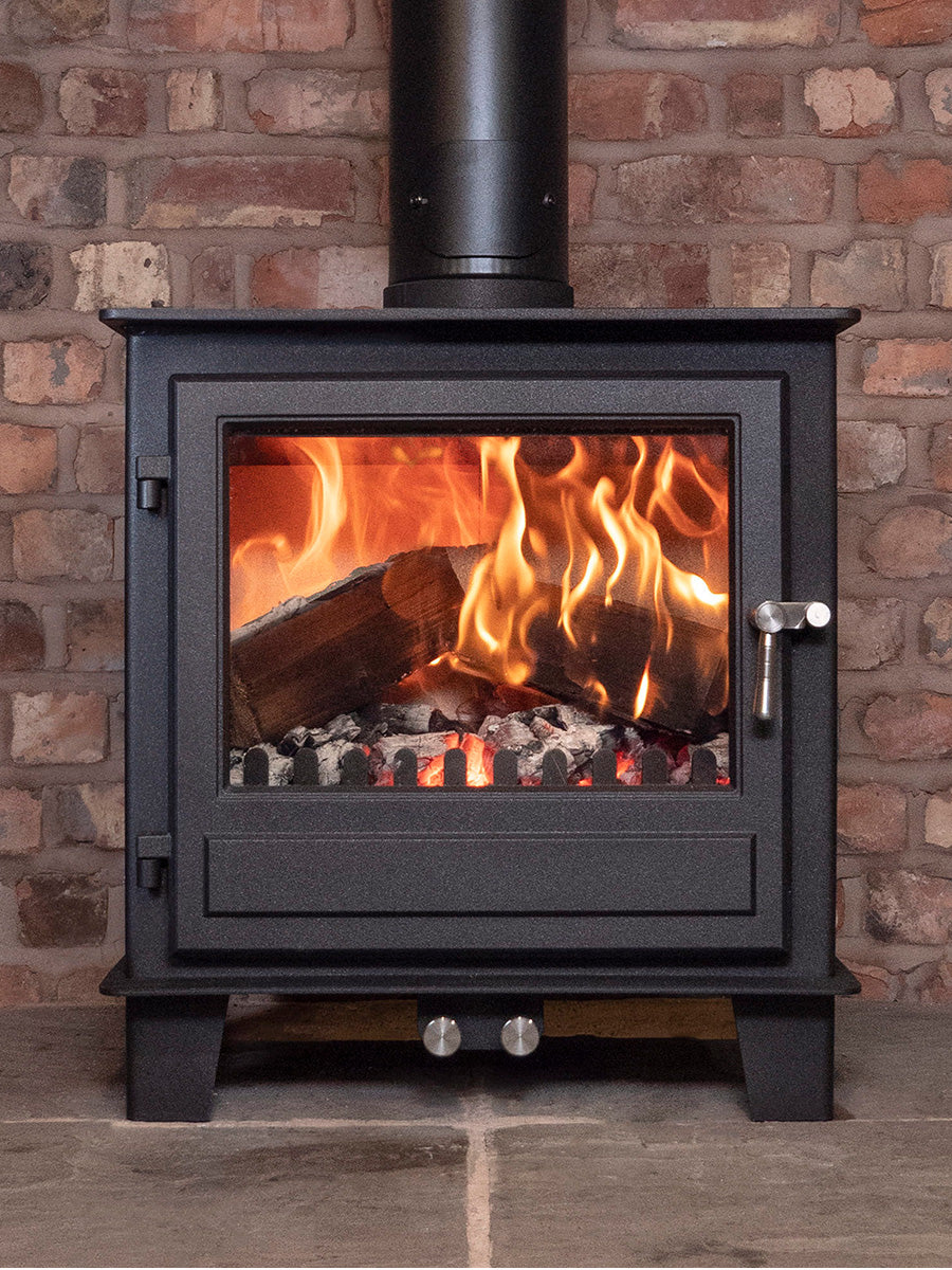 Black steel Clock Blithfield 8 wood burner with large glass panel, showcasing flames, in a cozy living room setting.