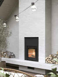Side view of the Contura i2 wood burning fireplace insert with a cast iron door and glass front, showcasing its compact design.