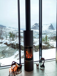 Side view of the RAIS PILAR wood-burning stove showcasing its curved glass and sleek metal design.