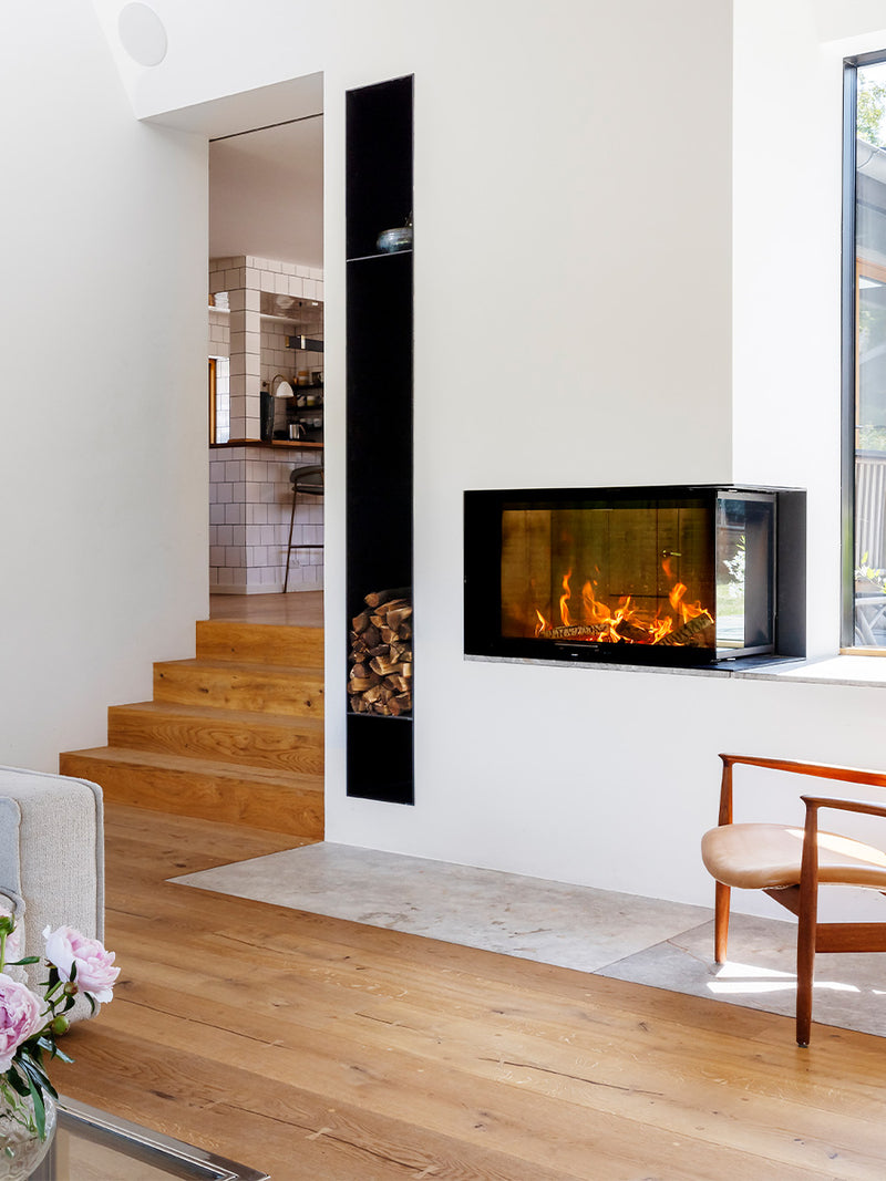 Large corner wood burning stove with sleek black frame and extra-large glass panes showcasing the fire inside.