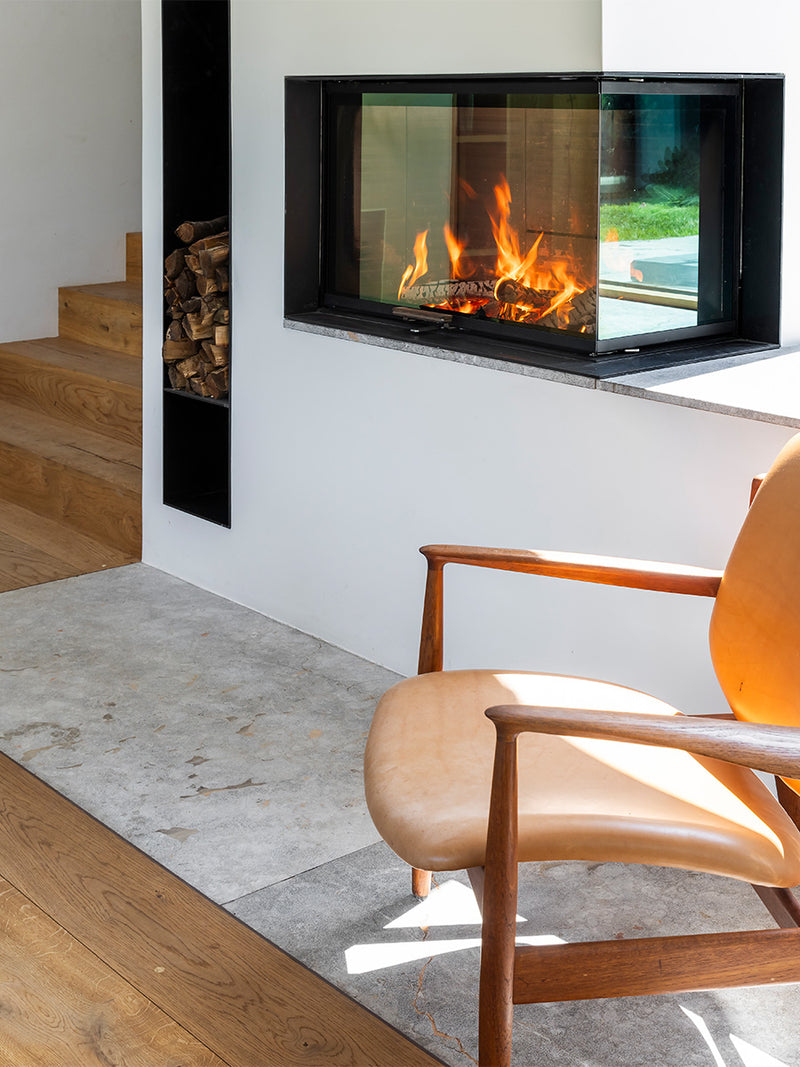 Side view of RAIS Visio 2 wood burning stove with large glass panes and sleek black frame, set in a corner.
