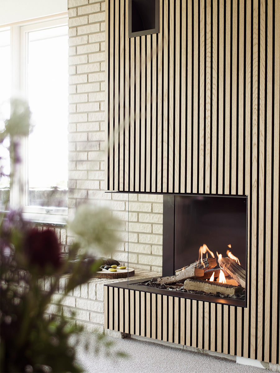 Corner gas fireplace insert with glass sides, black frame, showcasing realistic flames in a cozy setting.