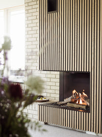 Corner gas fireplace insert with glass sides, black frame, showcasing realistic flames in a cozy setting.