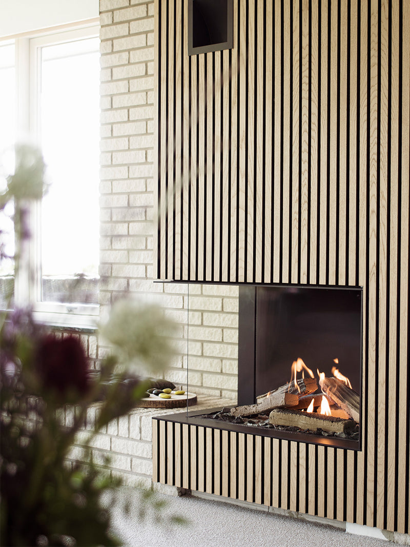 Corner gas fireplace insert with glass sides, black frame, showcasing realistic flames in a cozy setting.