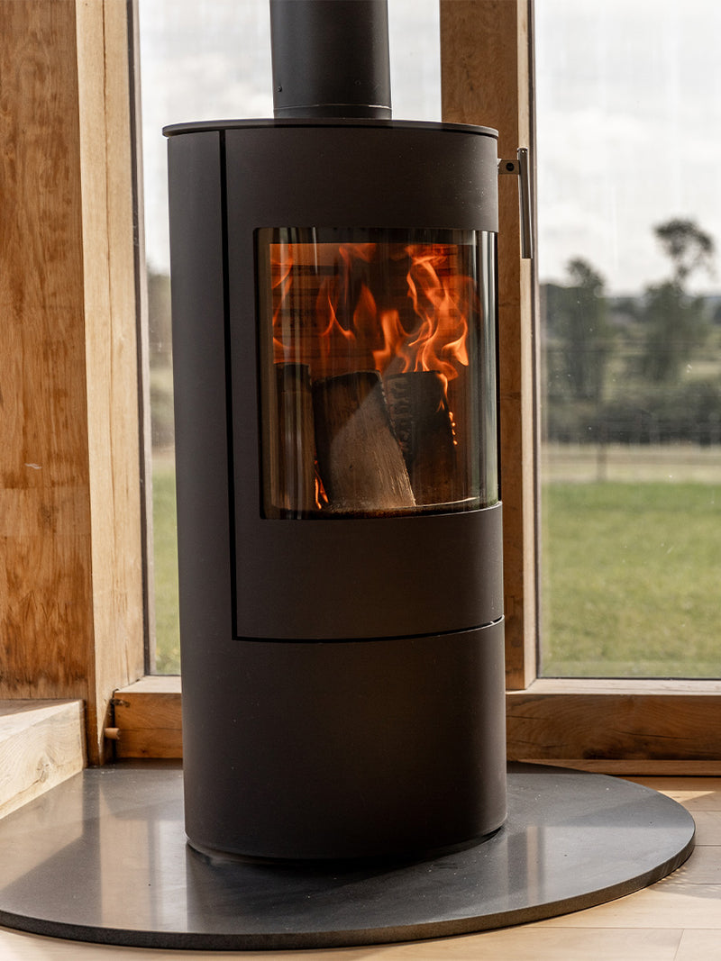 Side view of the RAIS Viva L 100 wood burning stove with a glass door, showcasing its curved design and sleek finish.