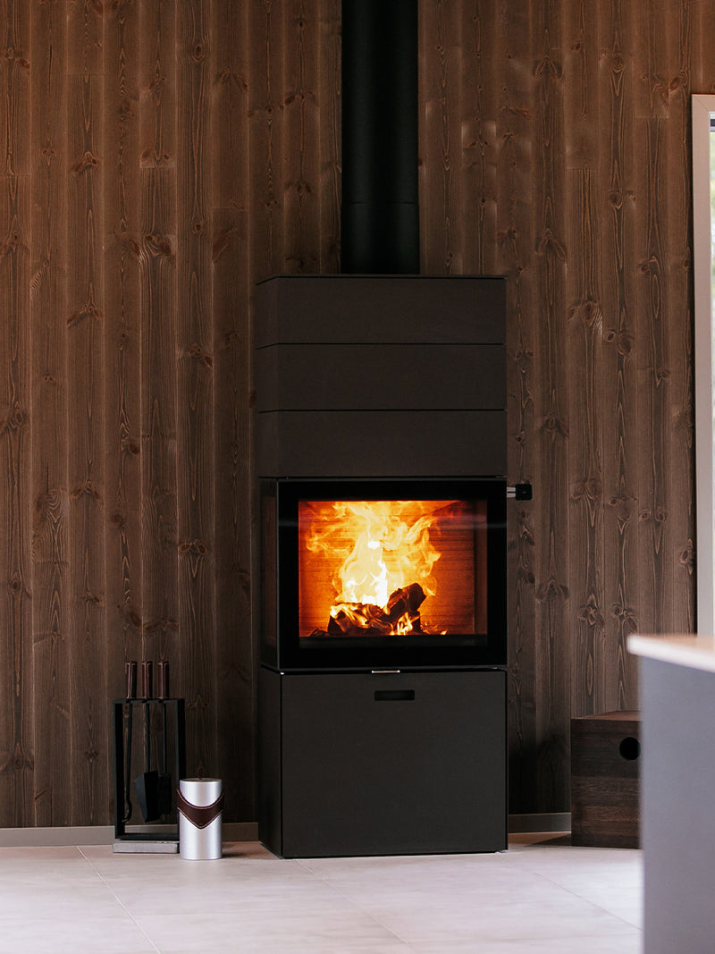 Side view of the RAIS 600 Max wood burning stove with glass door and three storage boxes in a sleek black finish.